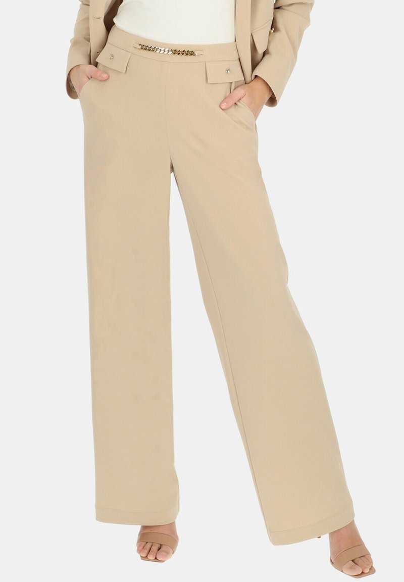 Beżowe spodnie o szerokich nogawkach z gładką fakturą, z przednimi kieszeniami, złotym akcentem łańcucha na pasku oraz dopasowanym krojem.