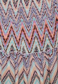 Mehrfarbiger Stoff mit einem Zickzackmuster in den Farbtönen Lila, Blau, Koralle und Pfirsich, mit gerafften Kanten am unteren Rand und einem Smocking-Detail.