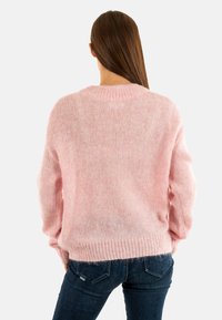 Maglione rosa lavorato a maglia con una vestibilità ampia, caratterizzato da un colletto rotondo a costine e maniche lunghe. La texture morbida si abbina perfettamente a jeans casual.
