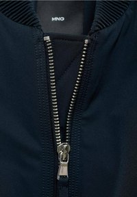 Giacca bomber blu navy con zip metallica, colletto a coste e texture del tessuto liscia con dettagli di cucitura visibili.