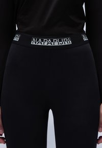 Czarne legginsy z szerokim pasem w kontrastowym białym logo "Napapijri". Materiał wydaje się gładki i elastyczny.