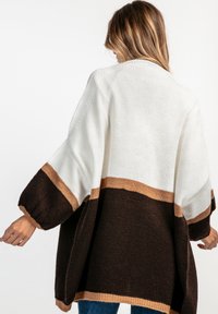Oversized kardigan w kremowych, brązowych i beżowych odcieniach. Posiada długie, szerokie rękawy, teksturowany wzór dzianiny oraz luźny krój.