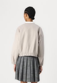 Lys beige jakke med sammensamlet forneden og løs pasform, parret med en grå plisseret nederdel. Simpelt design, glat tekstur og minimale detaljer.
