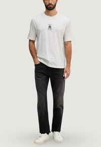 T-shirt à manches courtes en coton rayé blanc et marine, avec un logo sur la poitrine. Associé à un jean noir en denim et des baskets blanches.