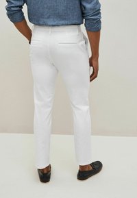 Chinos bianchi dal taglio slim, con tasche posteriori e una texture liscia. Abbinati a mocassini neri, visti da dietro.
