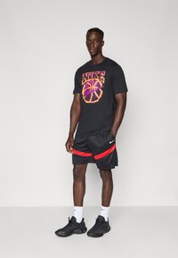 Sort Nike t-shirt med en orange og lilla basketball grafik, parret med sorte shorts med røde striber og sorte atletiske sko.