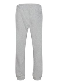 Lys grå joggebukser laget av mykt materiale, med elastisk liv, smale mansjetter og en enkelt baklomme. Enkelt design.