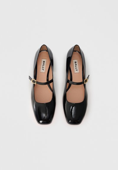 Chaussures plates en cuir verni noir avec un bout carré et une bride Mary Jane, dotées d'une boucle en or et d'une semelle intérieure lisse beige.