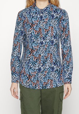 Femme portant une chemise à manches longues avec un motif abstrait bleu, noir, blanc et orange, accompagnée d'un pantalon cargo vert olive.
