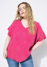 Top rosa testurizzato con scollo a V e maniche corte, caratterizzato da un taglio loose fit e orlo arrotondato, abbinato a jeans blu.