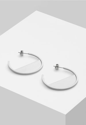 Pair of silver-toned open hoop earrings with post and butterfly fastenings displayed on a white angled surface.