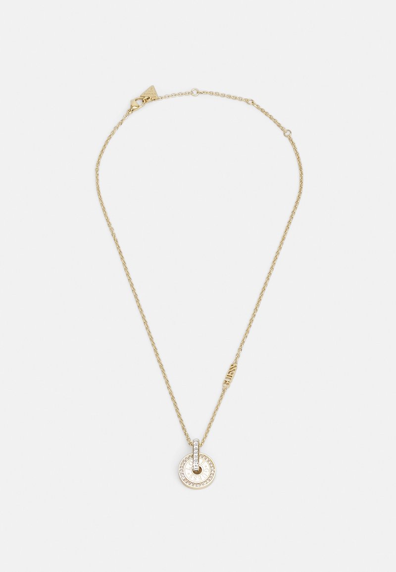 Collier en chaîne dorée avec un pendentif circulaire incrusté de petits cristaux et un petit charme logo le long de la chaîne sur fond blanc.