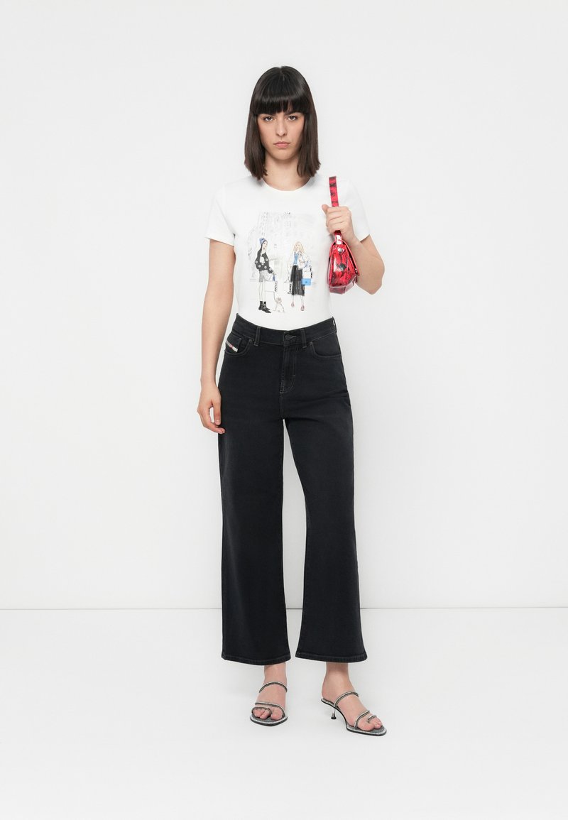 T-shirt graphique blanc avec design de dessin animé, jean noir taille haute à jambe large, sandales noires brillantes et un petit sac à main rouge.