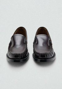 Mocasines de cuero negro con superficies lisas, detalles cosidos y punta redondeada. Interior con forro marrón. Suela plana negra.