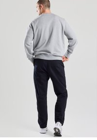 Grey sweatshirt with ribbed cuffs and hem, paired with navy sweatpants. The model wears white athletic shoes. Back view. Smooth texture.