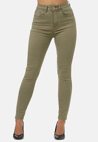 Jeans skinny de talle alto en verde olivo con cinco bolsillos y pasadores para cinturón, confeccionados con una tela elástica. Llevados con tacones negros.