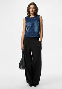 Jeansärmlös topp med blå tvätt, dekorerad med silvernitar; parat med högmidjade svarta vida byxor och en svart väska.