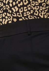 Ceinture en tissu noir avec une texture lisse, au-dessus d'un haut à imprimé léopard présentant une surface duveteuse et texturée dans des couleurs beige et marron foncé.