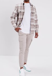 Geruit shirt in lichtbruin en wit, beige cargobroek met zakken, en witte sneakers met groene accenten. Glad materiaal en slim fit ontwerp.