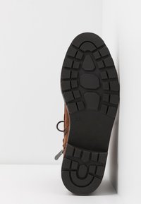 Semelle en caoutchouc noir avec des crampons profonds sur une botte marron, vue de dessous sur fond blanc, taille 37 indiquée sur la semelle.