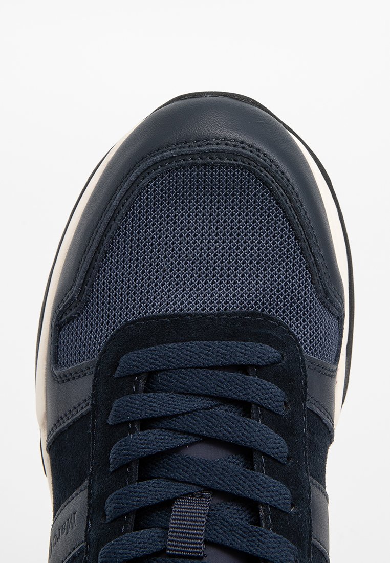 Widok z góry na granatowy sneaker z panelami z siatki, skóry i zamszu oraz pasującymi granatowymi sznurówkami na białym tle.