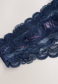 Dantelă bleumarin cu modele florale și margini zimțate, suprapusă pe un material neted cu o strălucire subtilă și accente roz.