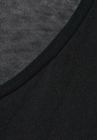 Nahaufnahme eines schwarzen strukturierten Stoffes, der eine gebogene Naht und ein Strickmuster mit feinen, eng gewebten Fasern zeigt.