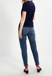 Granatowa koszula z krótkim rękawem w połączeniu z luźnymi niebieskimi dżinsami. Obuwie z czarnym paskiem z czerwonym akcentem. Prosty, casualowy design.