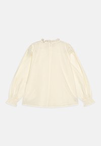 Blusa beige a maniche lunghe con scollatura e polsini volants. Presenta una chiusura con bottoni sul retro e un tessuto morbido e testurizzato.