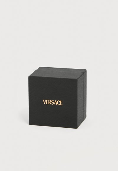 Μαύρο κουτί Versace με χρυσά γράμματα σε απλό ανοιχτό φόντο, τοποθετημένο ελαφρώς γωνιακά προς τα δεξιά.