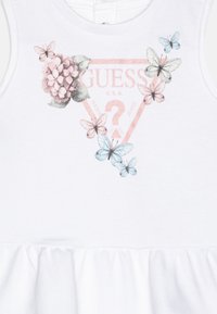 Biała sukienka bez rękawów z marszczonym dołem, ozdobiona kwiatowymi i motylkowymi nadrukami w różu i błękicie, z logo "GUESS" na piersi.