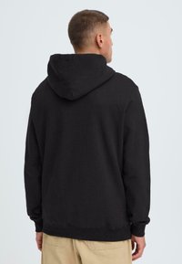 Zwarte hoodie met een relaxte pasvorm, voorzien van een trekkoordcapuchon, ribgebreide manchetten en zoom. Gemaakt van zacht katoen, minimalistisch ontwerp.