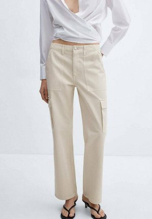 Woman wearing beige straight-leg cargo pants with patch pockets, a white wrap blouse, and black open-toe heeled sandals.
