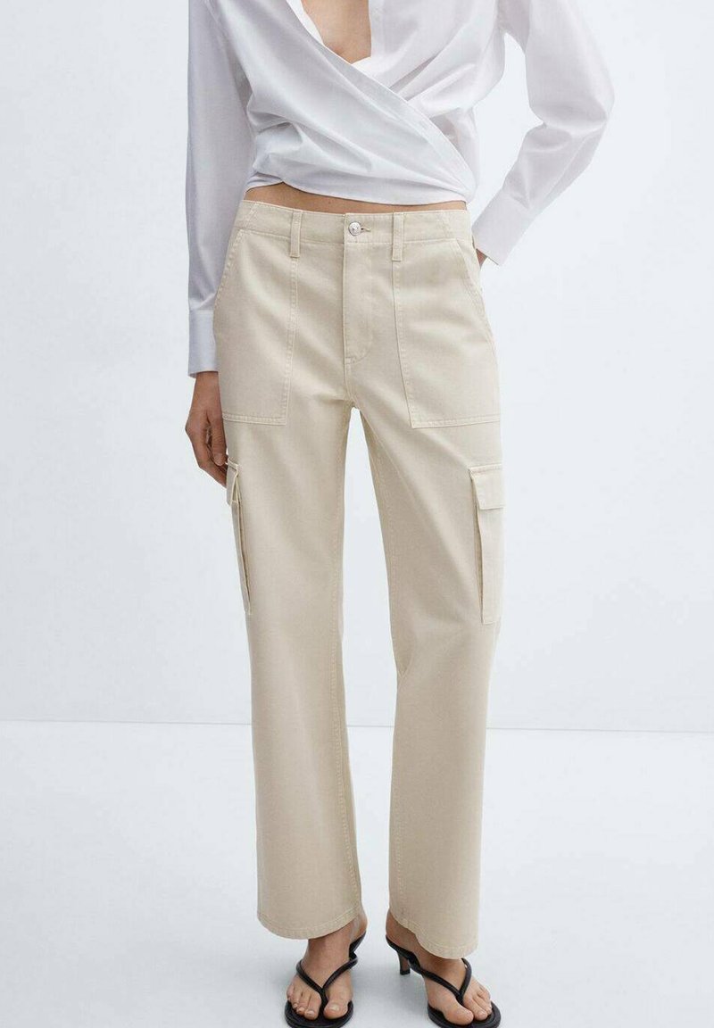 Woman wearing beige straight-leg cargo pants with patch pockets, a white wrap blouse, and black open-toe heeled sandals.