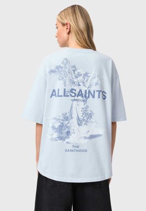 Kvinde iført en lyseblå oversized T-shirt med et englegrafik og teksten "ALLSAINTS LONDON THE SAINTHOOD" på ryggen.