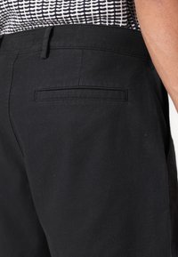 Pantalons en mélange de coton noir avec une texture lisse, coupe droite et une poche arrière. La taille est dotée de passants de ceinture pour un ajustement réglable.
