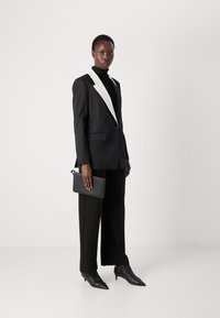 Black tailored suit with white lapels, worn over a black turtleneck. Black wide-leg trousers and pointed black ankle boots. Slim clutch bag.