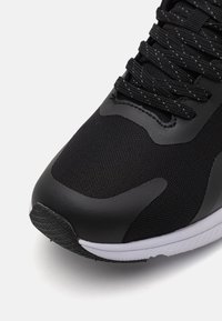 Chaussure de sport noire avec un dessus en maille texturée, des superpositions synthétiques et une semelle intermédiaire blanche. Elle présente des lacets noirs et une semelle extérieure en caoutchouc à motif.