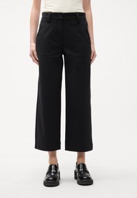 Sorte bukser med vide ben og høj talje, lavet af glat stof. Har bæltestropper og et skræddersyet design. Bruges sammen med sorte loafers.