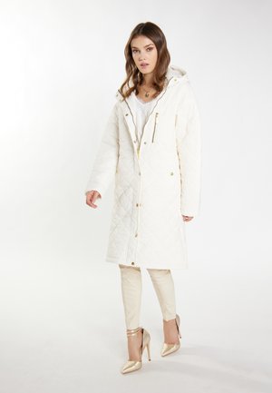 Gequilte witte lange jas met een capuchon, gouden hardware en een rits aan de voorkant. Draagt over crèmekleurige slim-fit broeken en gouden hoge hakken. Soepele textuur.