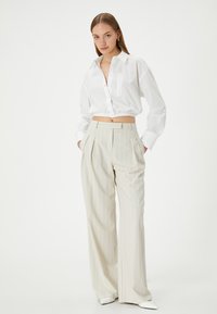 Camicia bianca croppata con bottoni e orlo elastico abbinata a pantaloni palazzo a righe beige chiaro. I pantaloni presentano pieghe frontali e tasche.