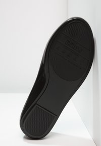 Suela de zapato de goma negra con textura acanalada, marcada "melissa". Presenta una superficie lisa y bordes redondeados, inclinada sobre un fondo blanco.