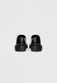 Sapatos pretos em pele envernizada com um acabamento suave, bico arredondado e solas grossas pretas. Apresentam um design minimalista, sem hardware ou detalhes visíveis.