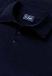 Granatowa koszulka polo z miękkiego materiału, z klasycznym kołnierzykiem, trzema ciemnymi guzikami oraz metką z napisem "Hackett London" na dekolcie.