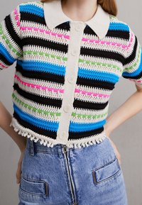 Stickad kofta med horisontella ränder i svart, blått, grönt, rosa och krämfärgat. Den har en krage, knäppning med knappar och franskant.