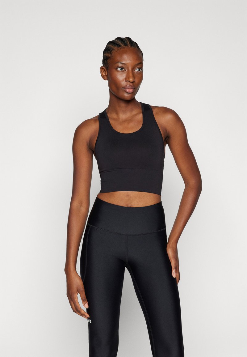 Sujetador deportivo negro cortado con tirantes anchos, combinado con leggings negros de cintura alta. Textura suave y diseño ajustado. Sencillo y funcional.