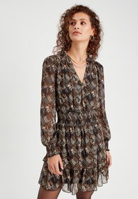 Robe imprimée avec un décolleté en V, des manches longues et une taille smockée. Présente un mélange de motifs floraux et géométriques dans des tons de marron et de crème.