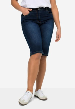 Mørkeblå denim bermudashorts med mellemhøj talje, forlommer og en let flosset kant, kombineret med hvide sneakers.