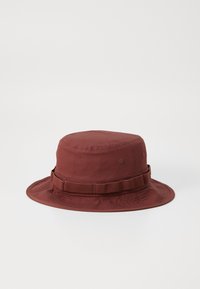 Burgundy bucket hat made of cotton with a flat crown, wide brim, and a textured fabric band around the base.