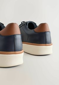 Sneaker in pelle blu navy con punta in pelle marrone, suola in gomma e dettagli testurizzati sulla mezze sole. Forma arrotondata e design minimal.